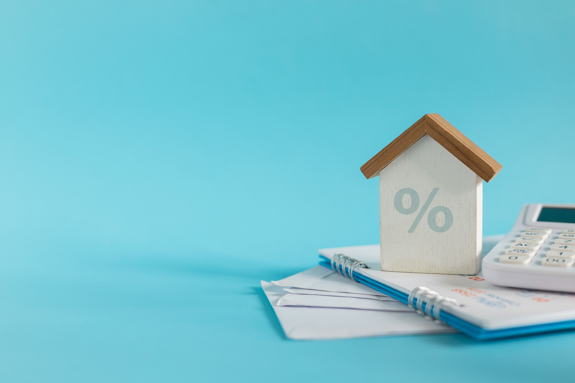 close up house model with percentage and bank statements with calculator on blue background for interest rate of home loan and refinance concept